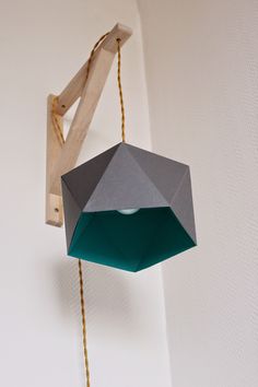 an origami birdhouse hanging from a string on the wall next to a piece of wood