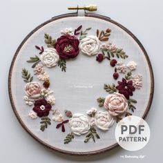 an embroidery pattern with flowers and leaves in the center on a white background, framed by a wooden hoop