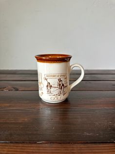 a white and brown coffee cup sitting on top of a wooden table next to a wall