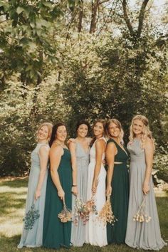 a group of women standing next to each other in front of some trees and bushes