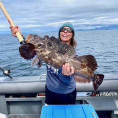 a woman on a boat holding a large fish with a fishing pole in her hand