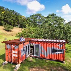 a man standing on top of a red shipping container next to a green field and trees