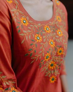 a woman wearing an orange top with yellow and green flowers on it's chest