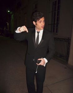 a man in a tuxedo points at something while standing on the sidewalk outside