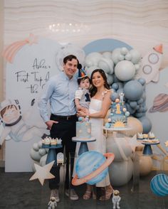 a man and woman holding a baby in front of a space themed backdrop with balloons