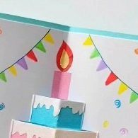 an open birthday card with a lit candle on the top and decorations around it,