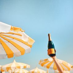 a person holding up a bottle of wine in front of umbrellas on the beach