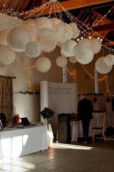 several white paper lanterns hanging from the ceiling above a table with people standing around it