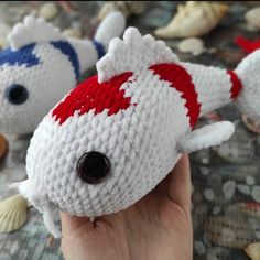 two knitted toy fish sitting next to each other on top of a table covered in seashells