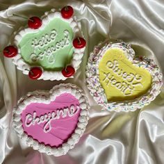 three decorated heart shaped cakes sitting on top of a white cloth covered table next to each other