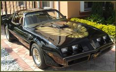 a black pontiac firebird parked in front of a house with gold eagle on the hood