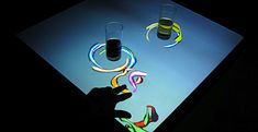 a person holding a cell phone in front of a lit up table with two glasses on it