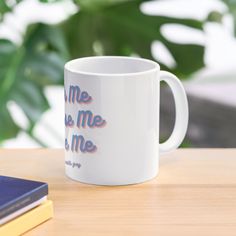 a white coffee mug sitting on top of a wooden table next to a blue book