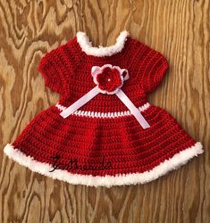 a crocheted red dress with white trim and a pink flower on the front