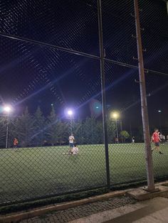 a group of people playing soccer on a field at night with the lights turned on