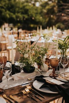 the table is set with white and gold plates, silverware, and greenery