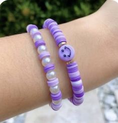 two purple and white bracelets with smiley face beads on each one arm, both decorated with pearls