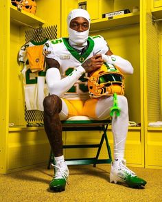 a man sitting in a locker room holding a football helmet and wearing a green and yellow uniform