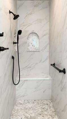 a walk in shower sitting next to a white tiled wall and floor with black faucets