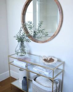 a table with a mirror and some plants on it in front of a white wall