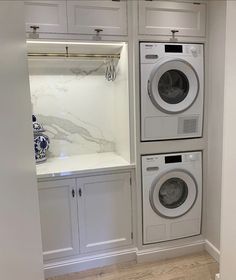 a washer and dryer are in the corner of this laundry room with white cabinets