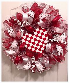 a red and white mesh wreath with a heart on the front door, decorated with bows