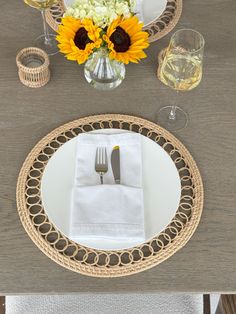 a place setting with sunflowers and silverware on a table cloth, next to wine glasses