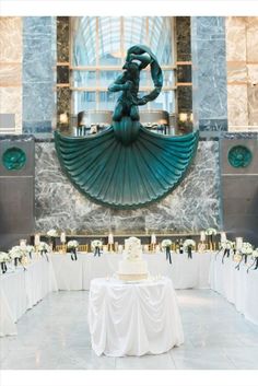 a wedding cake sitting on top of a table in front of a large wall sculpture