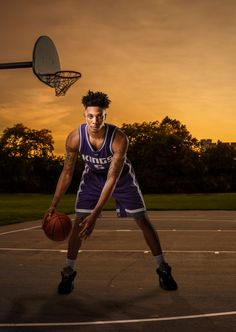 a man holding a basketball on top of a basketball court with the sun setting in the background