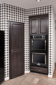 a kitchen with black and white checkered wallpaper, two ovens in the corner