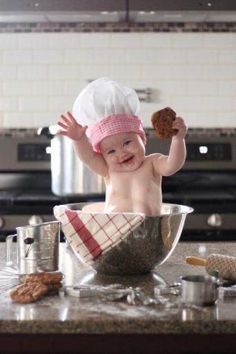 a baby is sitting in a bowl with some food on the counter and wearing a chef's hat