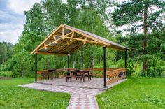 a picnic shelter in the middle of a grassy area with tables and benches under it