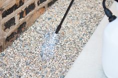 a white jug sitting on top of a gravel covered ground next to a brick wall