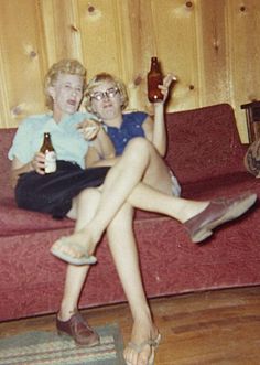 two women sitting on a couch with beer bottles in their hands and one holding a bottle