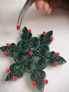 a hand holding scissors over an ornament made out of green and red paper