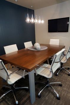 an empty conference room with white chairs and a wooden table in front of a flat screen tv