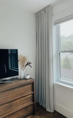 a flat screen tv sitting on top of a wooden dresser next to a large window