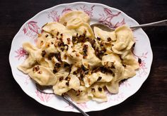 a white plate topped with dumplings covered in sauce and seasoning next to a spoon