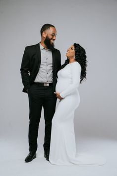 a man and woman standing next to each other in front of a gray background wearing black suits