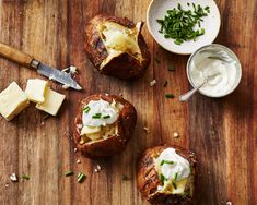 three baked potatoes with cheese and chives on a wooden cutting board next to butter