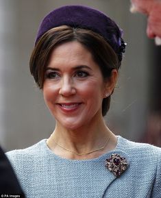 the queen is wearing a purple hat and smiling