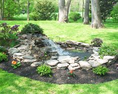 a small pond in the middle of a garden with rocks and flowers around it, surrounded by trees