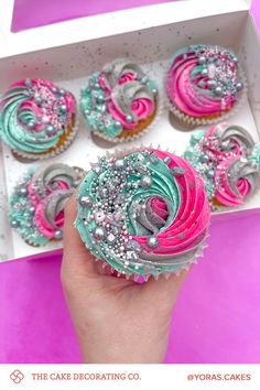 there is a box of cupcakes with pink, blue and silver frosting