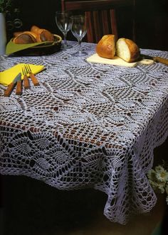 a crocheted tablecloth on a dining room table with bread and wine glasses