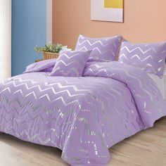 a bed with purple comforter and pillows on top of wooden floor next to pink wall