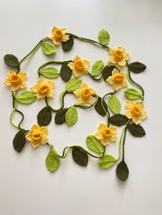 crocheted flowers and leaves are arranged on a white surface, with one yellow flower in the center