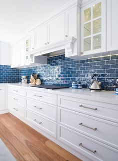 a kitchen with white cabinets and blue tiles on the backsplash is pictured in this image