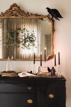 a black dresser topped with candles next to a mirror and a bird on top of it