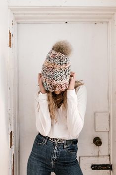 a woman in jeans and a white shirt is covering her head with a knitted hat