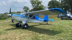 a blue and white plane sitting on top of a grass covered field next to a pick up truck